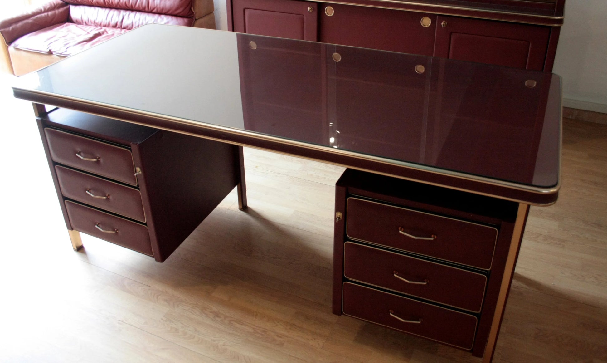 Scrivania ministeriale disegnata da umberto mascagni in similpelle bordeaux con piano in vetro e cassetti in bordeaux